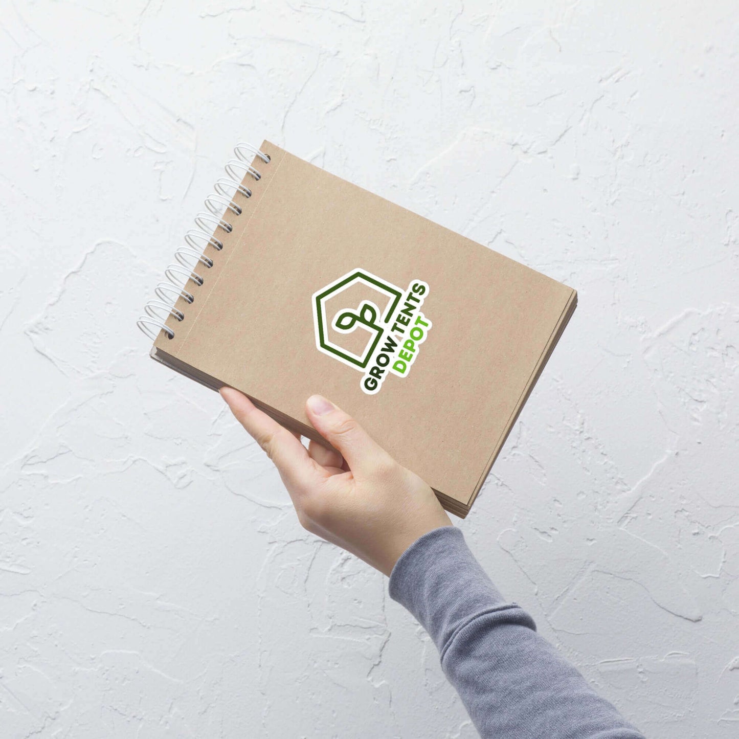 Person holding a notebook with Grow Tents Depot logo against a textured white wall.